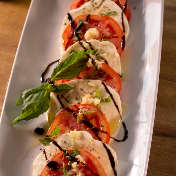 Caprese salad with sliced mozzarella, tomatoes, basil, garlic, and balsamic glaze on a white plate.