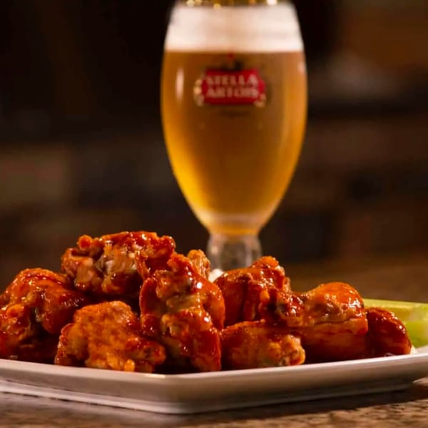 A plate of Mike's Pizza and Pub's buffalo wings with celery sticks and a Stella Artois beer.