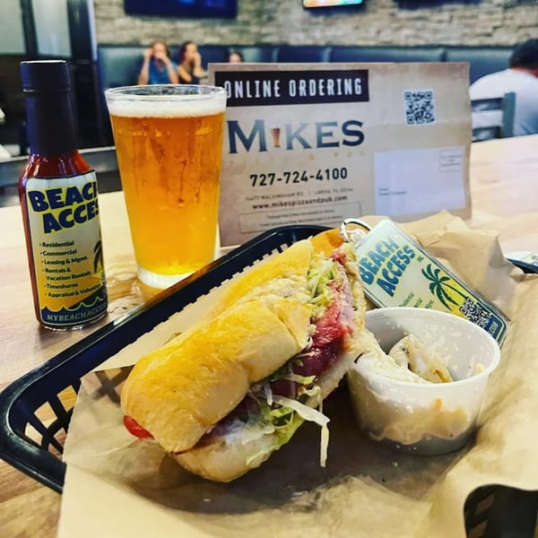 Mike's Pizza and Pub sub sandwich, side dish, beer, and hot sauce on a table.
