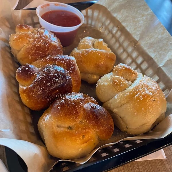 A basket of Mike's Pizza and Pub garlic knots, sprinkled with parmesan cheese, served with marinara sauce.