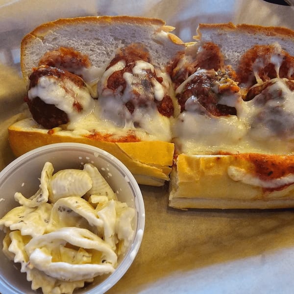 Meatball sub with melted cheese and marinara sauce, alongside a container of pasta salad.