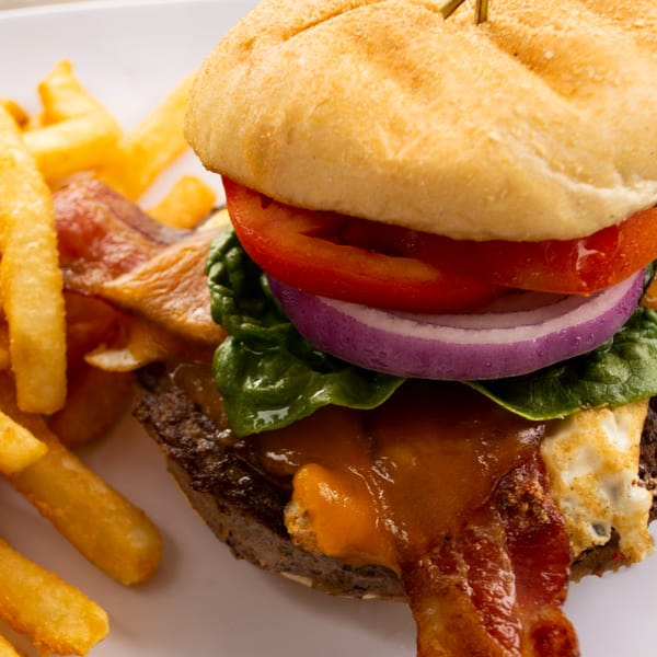 Close-up of a Mike's Pizza and Pub burger with bacon, cheese, tomato, onion, and spinach, with fries.