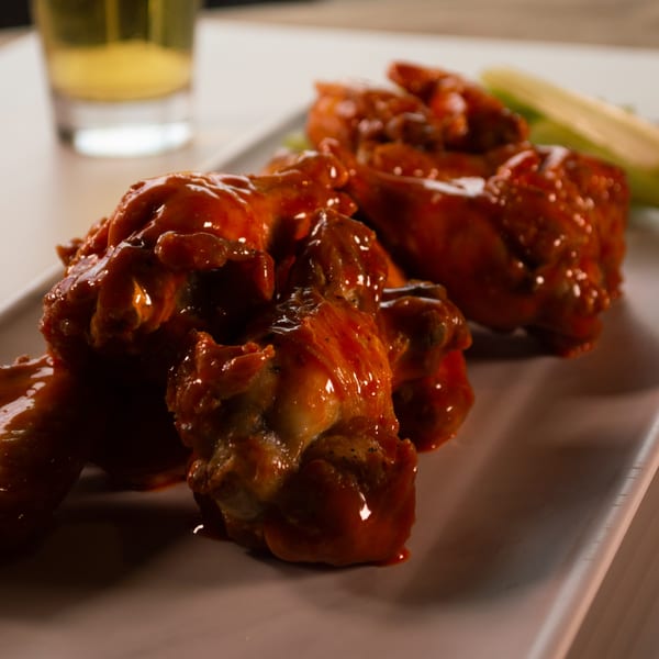 Mike's Pizza and Pub's buffalo wings, coated in a glossy red sauce, served with celery and a drink.