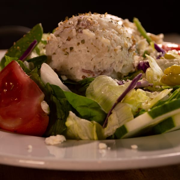 Close-up of a fresh Italian salad with lettuce, tomatoes, cucumbers, and a scoop of ricotta cheese.